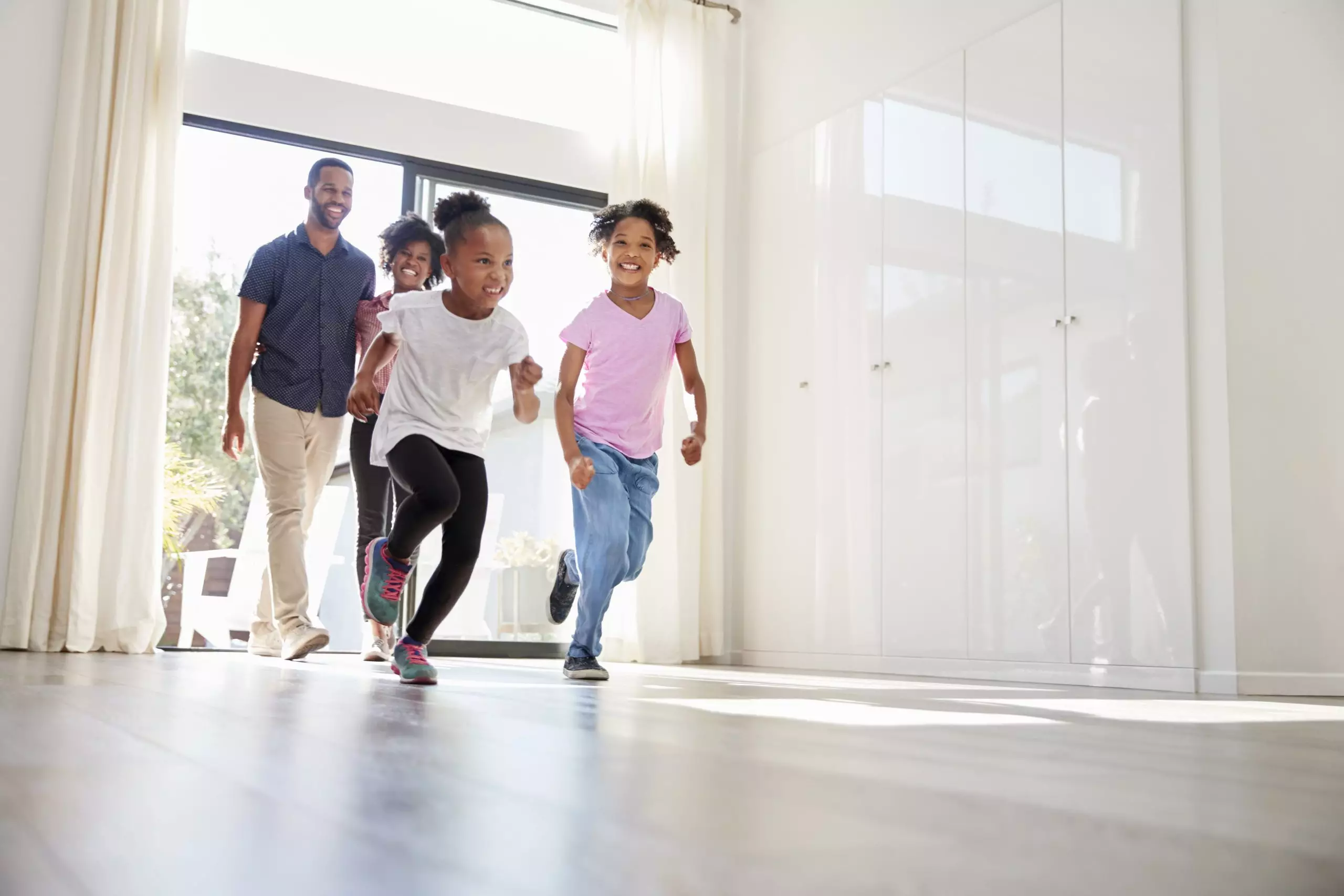 Happy Black family of four entering the sliding glass door to their empty, light, bright new home.