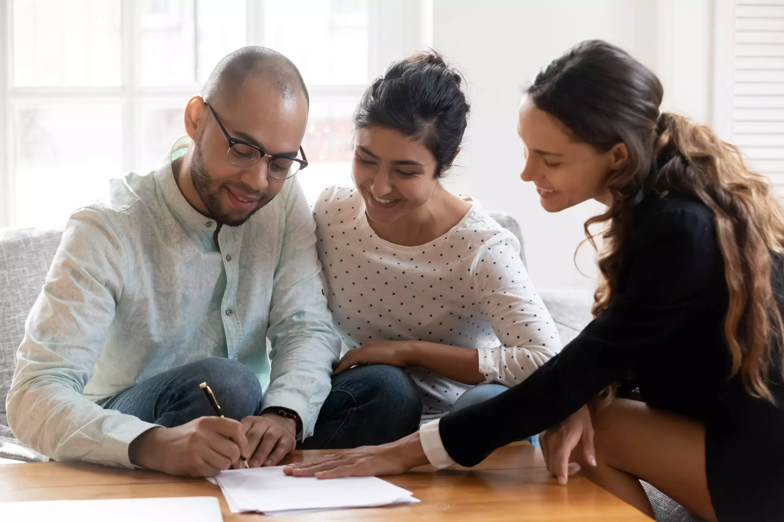 Young, smiling couple signing documents with a smiling female agent